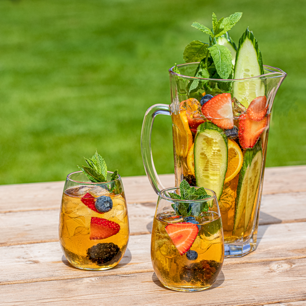pitcher of pimms with tw ofilled glasses on a bench